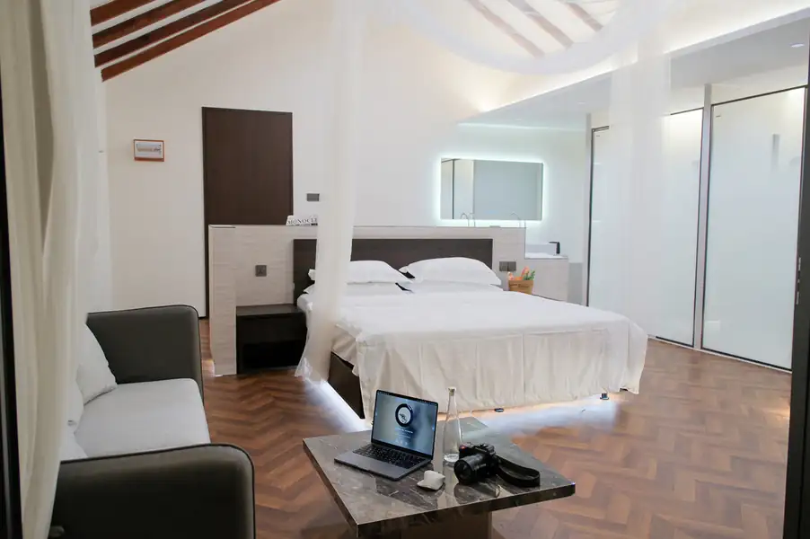 A spacious modern bedroom featuring a bed with a white mesh net, a sofa, and a marble coffee table holding a laptop and camera, embodying contemporary local design at Orange Wave Resort.