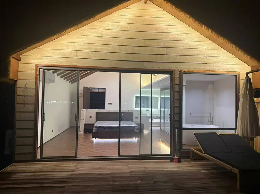 A luxurious overwater villa with expansive glass doors, a prominent thatched roof, and a wooden deck featuring a freestanding bathtub at Orange Wave Resort.